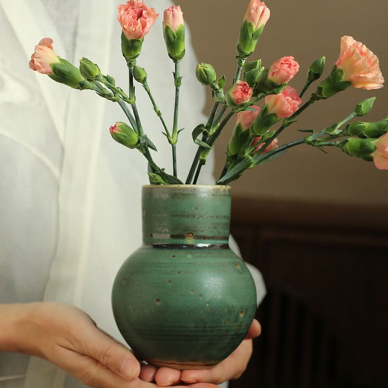 Small sage green ceramic vase holding pink carnations, home decor.
